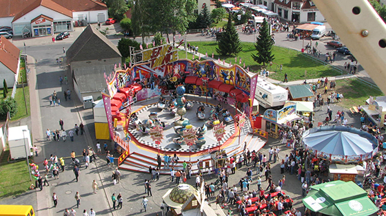 Ein Blick vom Riesenrad zeigt ein Fahrgeschäft des Hochzeitsmarkt, einem Volksfest in Kaltennordheim. Um das Fahrgeschäft stehen mehrere Menschen und Buden.