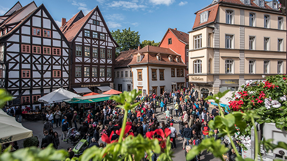 Ein Blick aus einem Fenster zeigt Menschen, die das Krämerbrückenfest besuchen. Im Hintergrund sind die Fachwerkhäuser von Erfurt zu sehen.