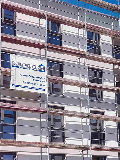 Ein Gerüst mit dem Banner der Josef Grund GmbH steht vor einem modernen Wohngebäude