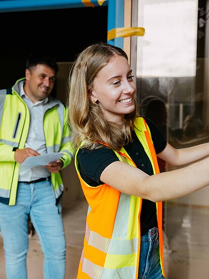 Mitarbeitende auf einer Baustelle im Innenausbau vermessen Arbeitschutzjacken tragend ein Wandstück