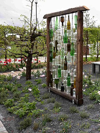 Sitzgelegenheiten umgeben von gestalteten Beeten und Pergola mit Flaschendekoration