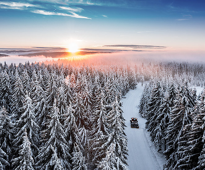 Der schneebedeckte Thüringer Wald von oben. Auf einem Weg fährt ein Schneemobil.