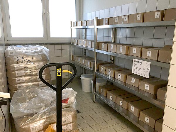 TAIAO-Kichererbsen-Lager mit Pappkartons in Metallregalen, gestapelte Säcke mit Rohstoffen und Hubwagen