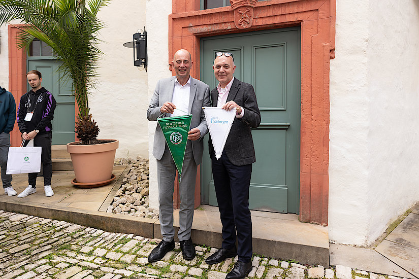 Minister Wolfgang Tiefensee hält einen grünen Wimpel mit der Aufschrift „Deutscher Fußball-Bund“ in den Händen. Daneben steht DFB-Präsident Bernd Neuendorf mit einem weißen Wimpel und der Aufschrift „Das ist Thüringen“ in der Hand.