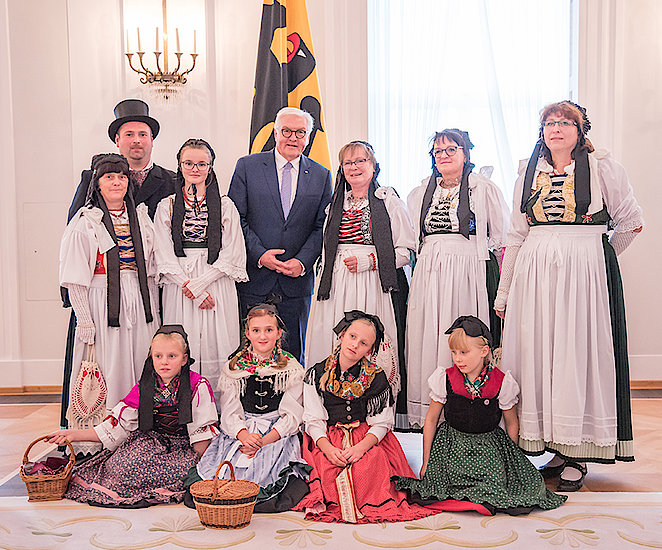 Ein Gruppenfoto von neun Leuten in der Tracht von Tabarz mit weißen Schürzen über ärmellosen Kleidern mit Schnürung und schwarzen Bändern im Haar. Der einzige Mann auf dem Bild trägt einen schwarzen Mantel und einen Zylinder. Sie stehen im Bundestag von Berlin und positionieren mit Frank Walter Steinmeier.