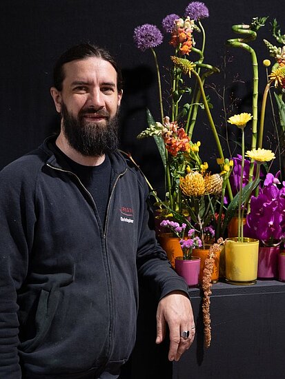 Christopher Ernst neben mehreren Blumenarrangements vor schwarzem Hintergrund