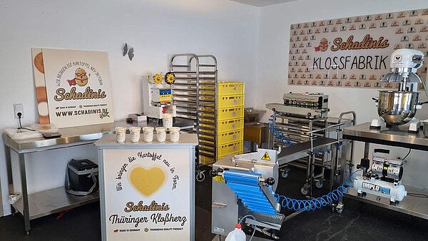 Schadinis Kloßfabrik mit Zubereitungsmaschinen und Laufband in einem Raum