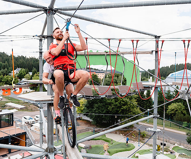 Max Langenhan fährt auf einem Fahrrad auf dem Kletterturm. Toni Eggert sitzt vorne auf dem Lenker. 