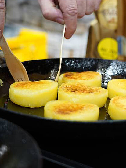 Kloßherzen werden in einer Pfanne goldbraun gebraten, daneben stehen die Kloßverpackungstüten aufgereiht