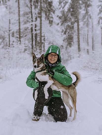 Anke Schiller-Mönch umarmt ihrem Schlittenhunde-Husky im verschneiten Thüringer Wald