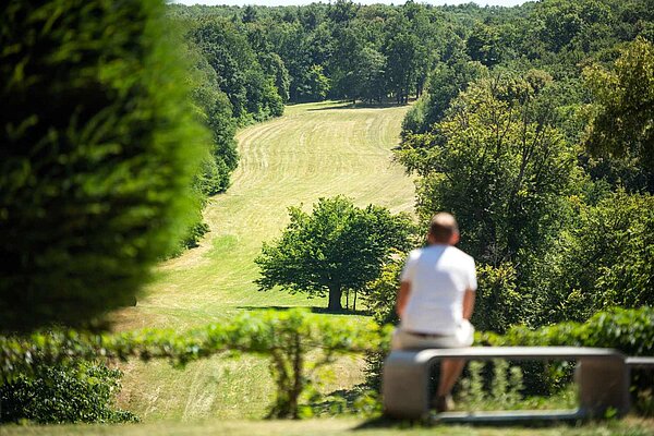 Besucher sitzt auf einer Bank im Schlosspark Ettersburg und schaut eine Sichtachse entlang