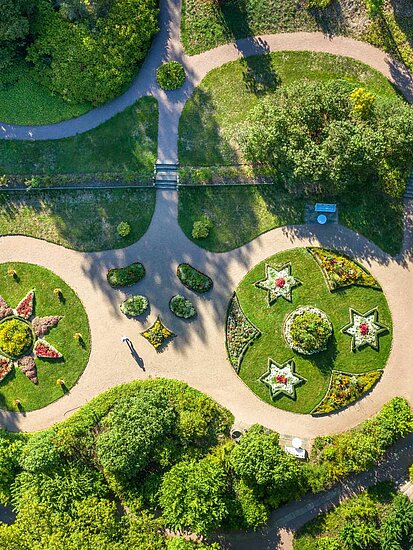 Luftaufnahme vom Blumengarten des Schlossparks Kochberg mit grünen Baumgruppen, geschwungenen Rasenflächen, Wegen und Beete mit Sternförmiger Bepflanzungen