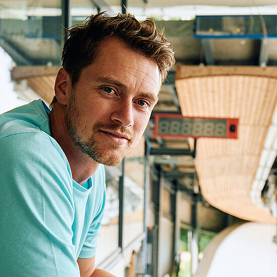 Johannes Ludwig steht am Herrenstart der LOTTO Thüringen EISARENA in Oberhof und lehnt an einer Brüstung, er blickt in die Kamera. Im Hintergrund sieht man die Startuhr.