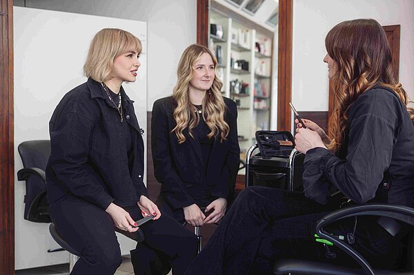 Drei junge Damen sitzen in einem Friseursalon und unterhalten sich