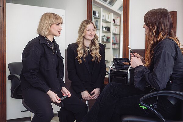Drei junge Damen sitzen in einem Friseursalon und unterhalten sich