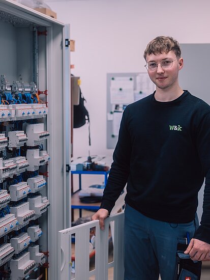 Ein junger Elektroniker steht vor einem Schaltschrank mit elektronischen Komponenten einer verfahrenstechnischen Anlage