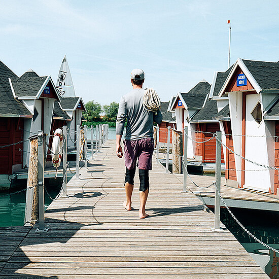 Johannes Ludwig auf dem Steg am Alperstedter See. Er hat ein Tau über seine Schulter gelegt. Rechts und links von ihm sind kleine rote Häuschen im Wasser.