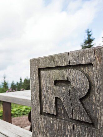 Rastplatz am Rennsteig mit Holzbank, in Holzblock eingraviertem "R" und Ausblick in die Landschaft und in den Horizont