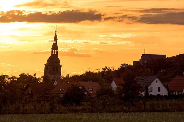Ein massiver steinerner romanischer Kirchturm mit barocker Turmhaube steht vor einem Himmel in der Abenddämmerung