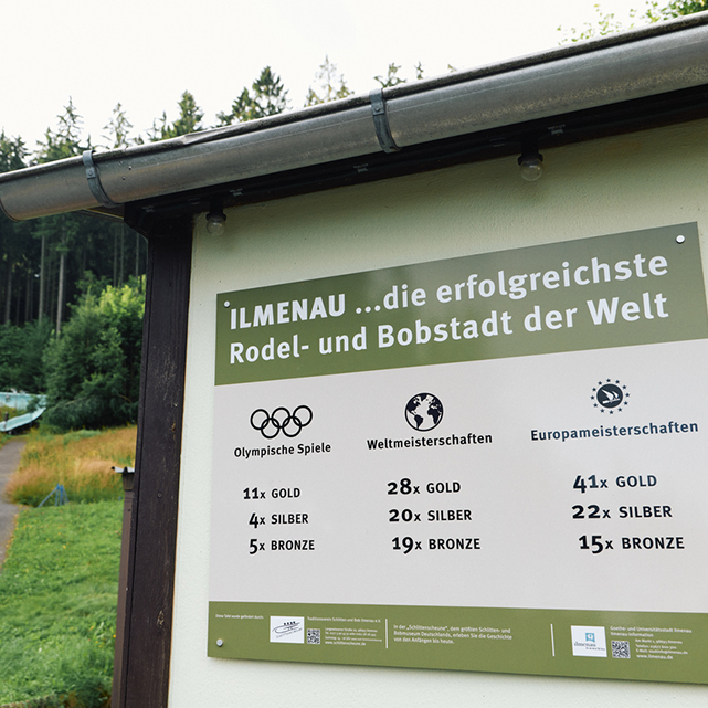 Eine Infotafel über Ilmenau, die erfolgreichste Rodel- und Bobstadt der Welt. Aufgelistet sind diverse Erfolge, die Rodler und Bobfahrer der Stadt errungen haben.